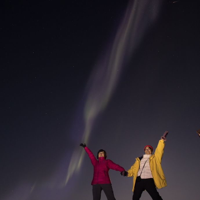 Two people with joining hands other arms up to the sky under the aurora - northern lights